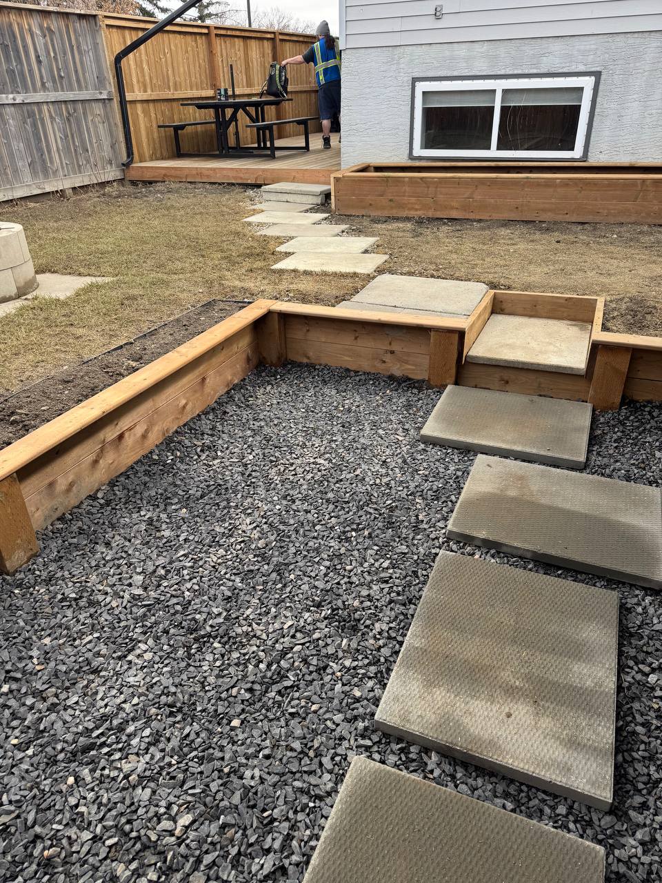 Completed backyard hardscape with gravel base, stepping stones, wooden planter boxes, and built-in s