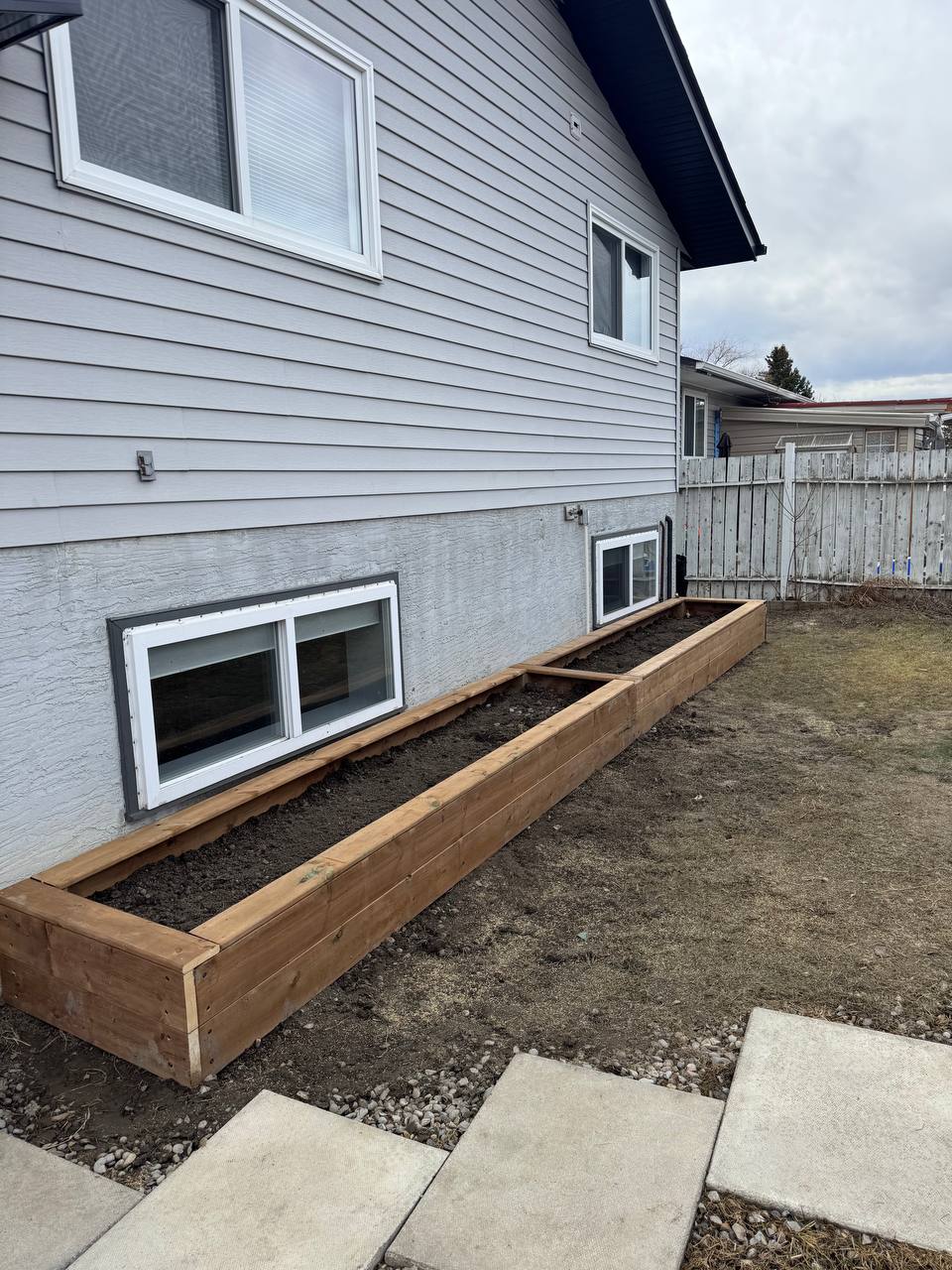Newly installed wooden retaining wall with landscape fabric and dark mulch along house foundation