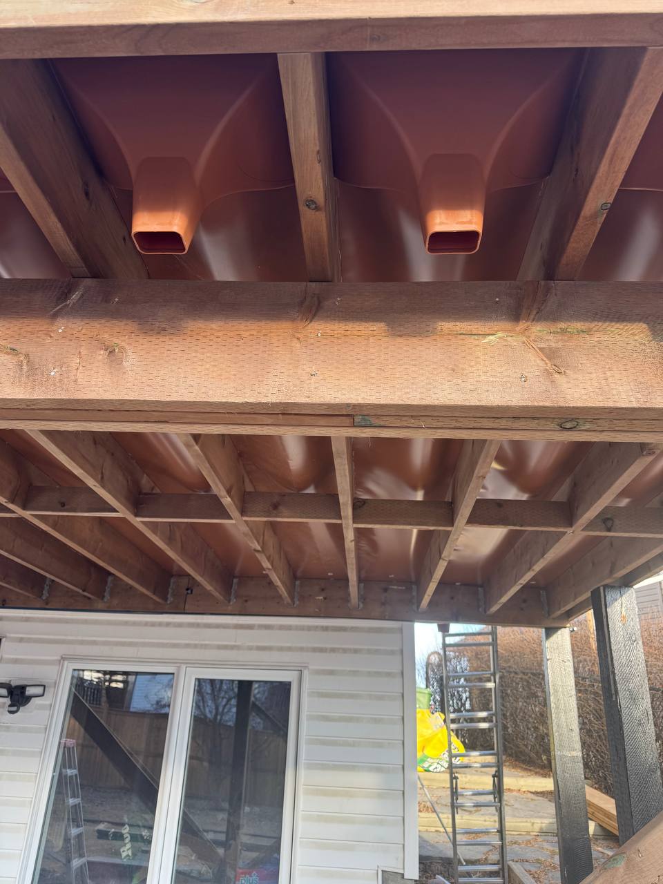 Pergola construction in progress with framing and copper downspout installation visible