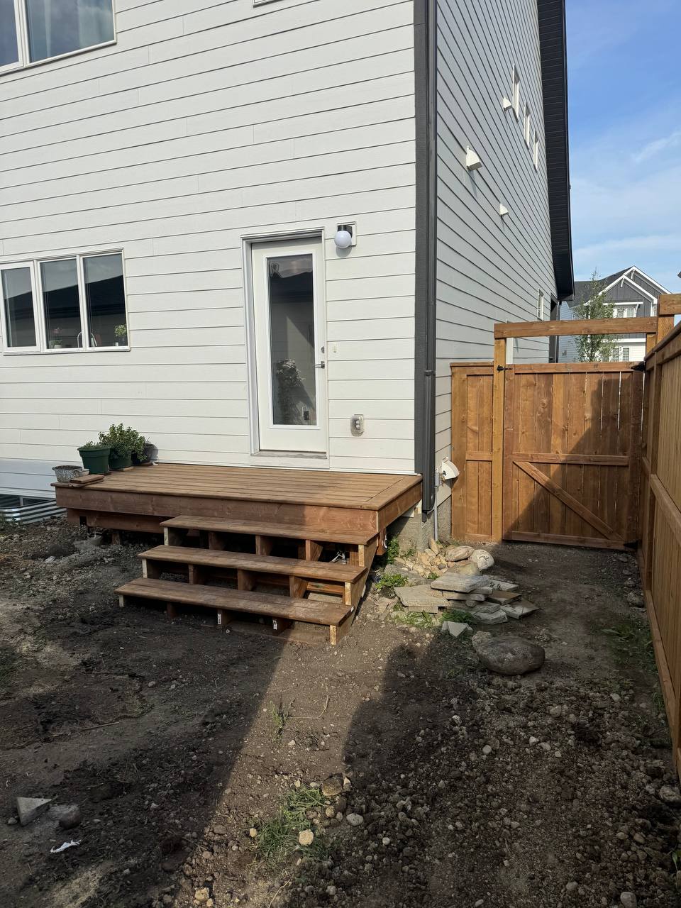Newly constructed wooden deck with stairs attached to modern residential home with fenced backyard