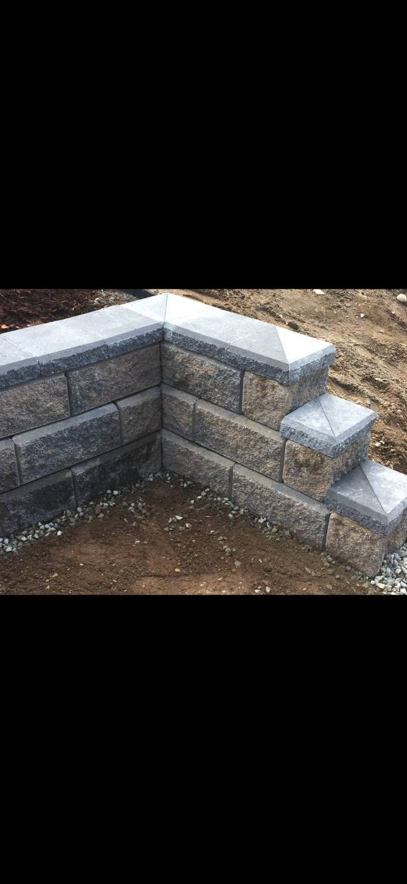 Completed concrete block retaining wall with cap stones and gravel base in landscape setting