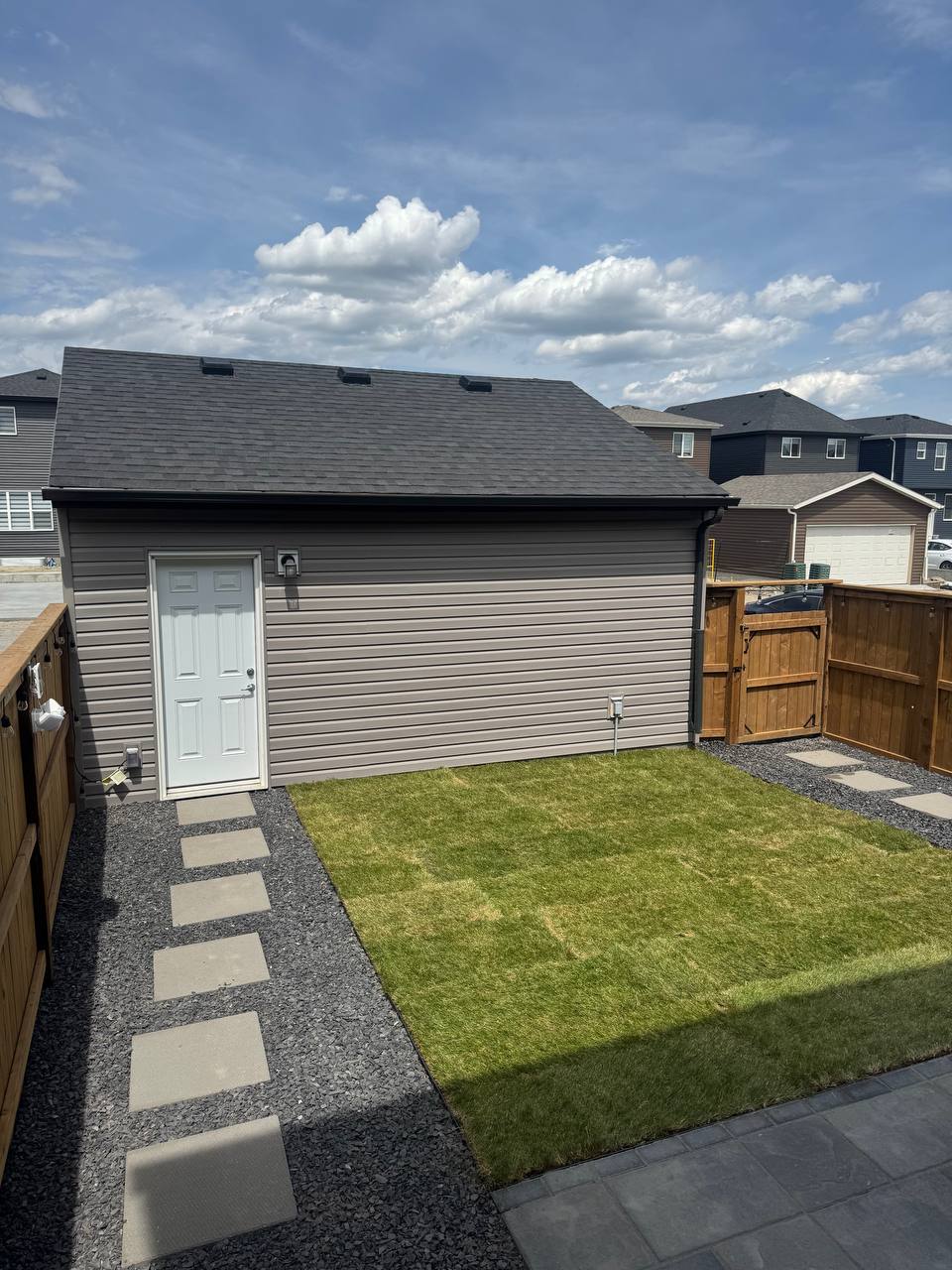 Completed backyard with stepping stones, gravel, sod, and wooden fence surrounding detached garage s