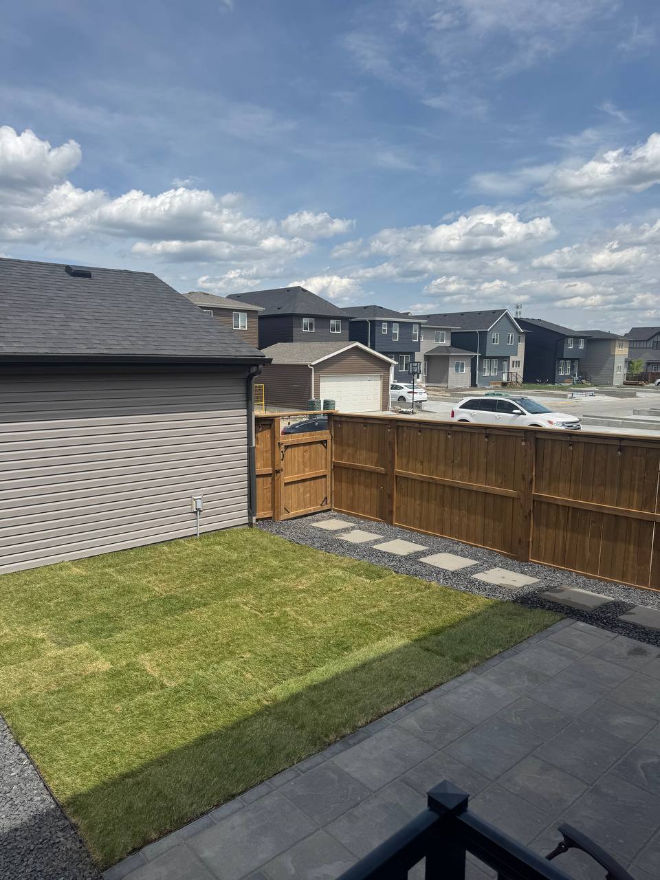 Completed backyard hardscape with patio, stepping stones, and wooden fence in residential neighborho
