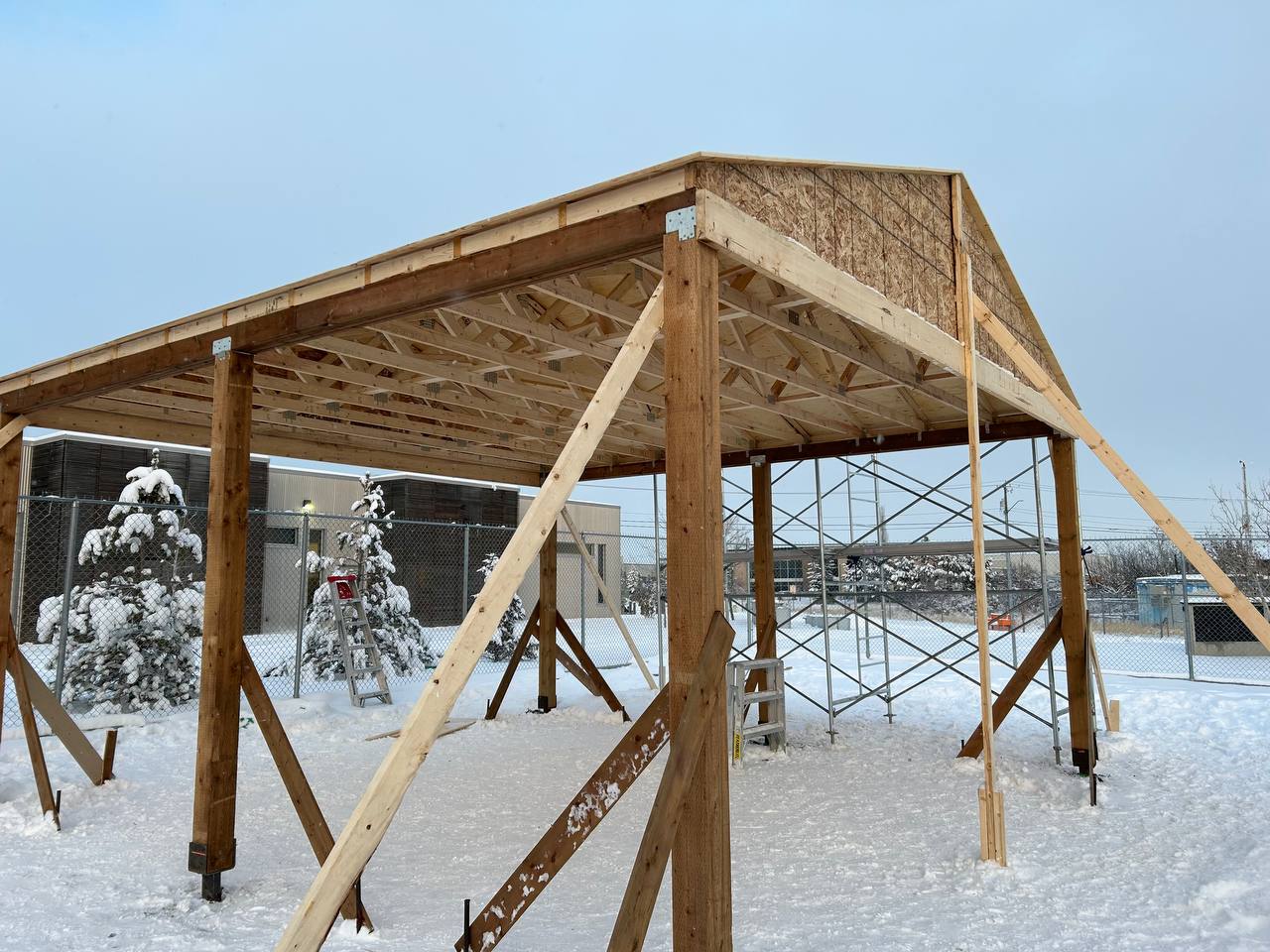 Wooden pergola structure under construction in snowy conditions with exposed framing and bracing vis
