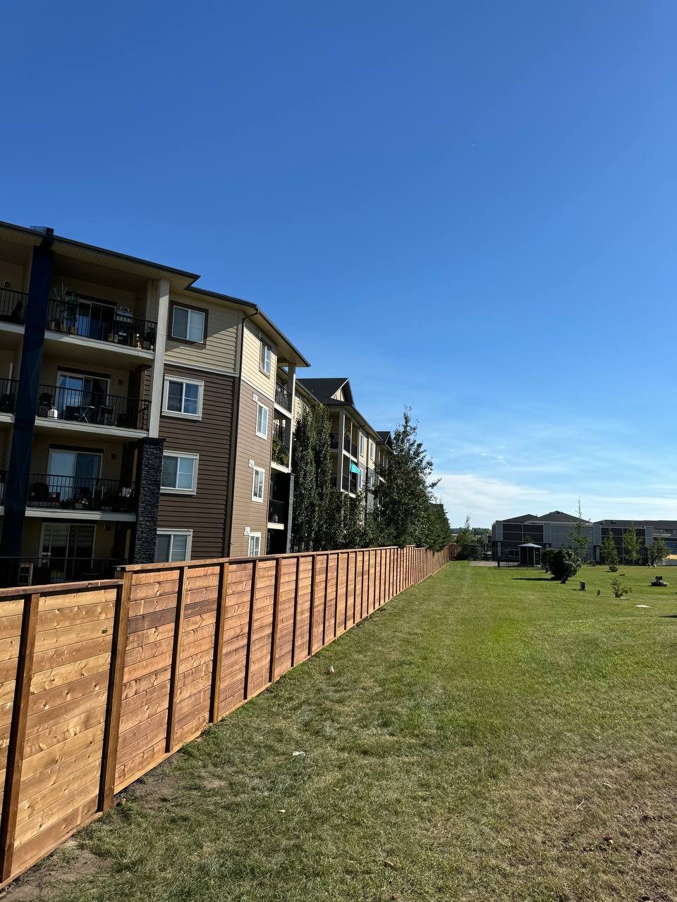 Newly installed wooden privacy fence along residential apartment complex with manicured lawn