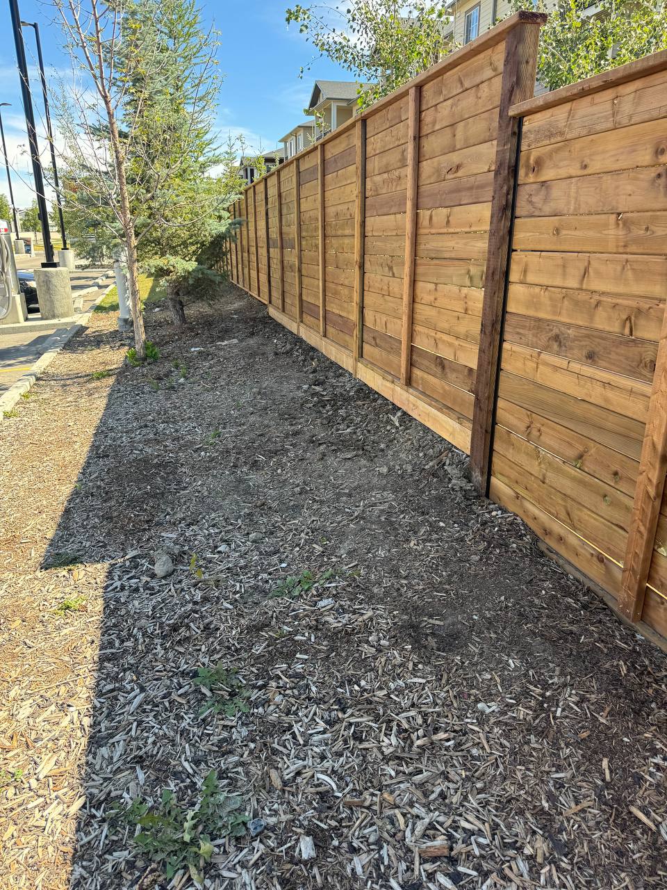 Newly installed horizontal wood fence with dark stain and mulched landscaping base