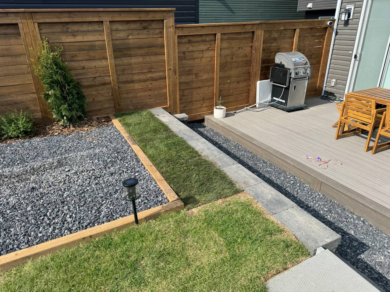 Completed backyard landscaping with composite deck, sod, gravel beds, and wooden fence