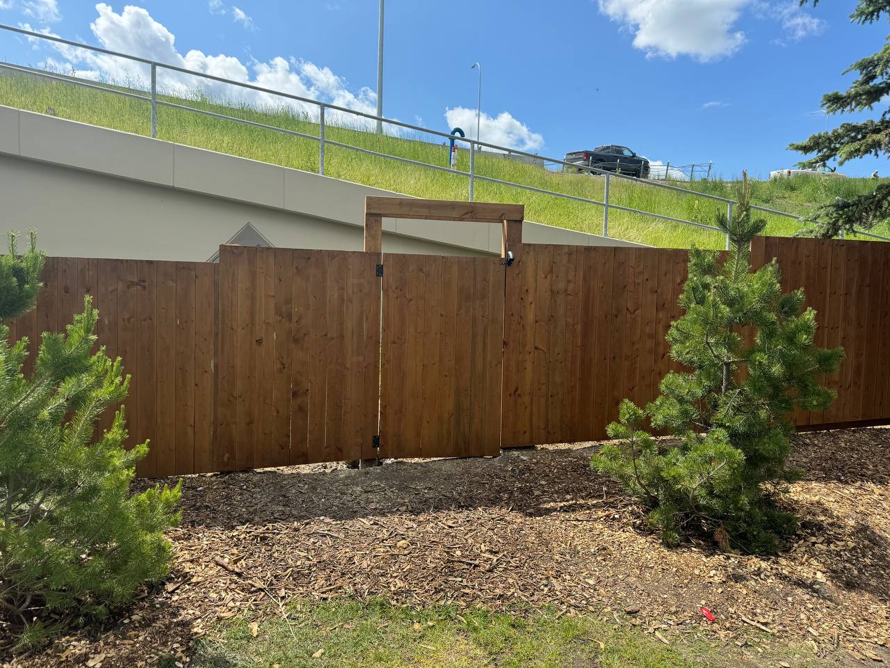 Completed wooden privacy fence installation with gate in landscaped yard below retaining wall