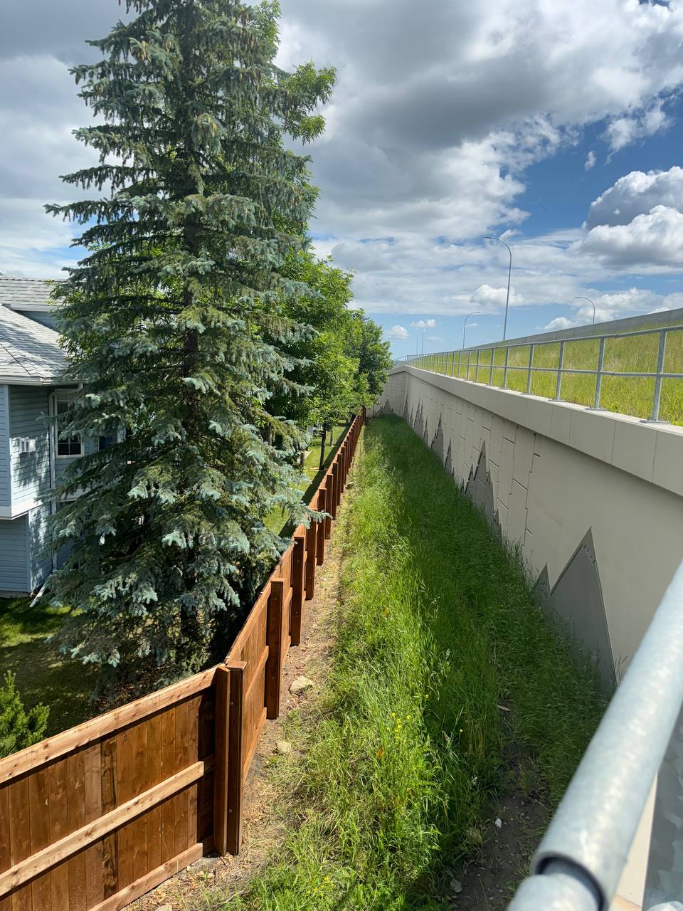 Completed concrete retaining wall installation with wooden fence and mature evergreen landscaping