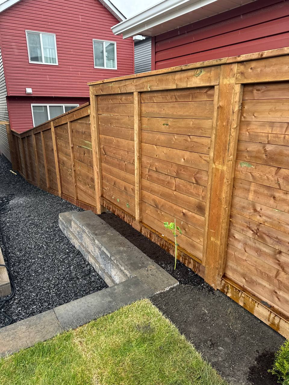Completed wooden privacy fence installation with horizontal boards and concrete foundation along res