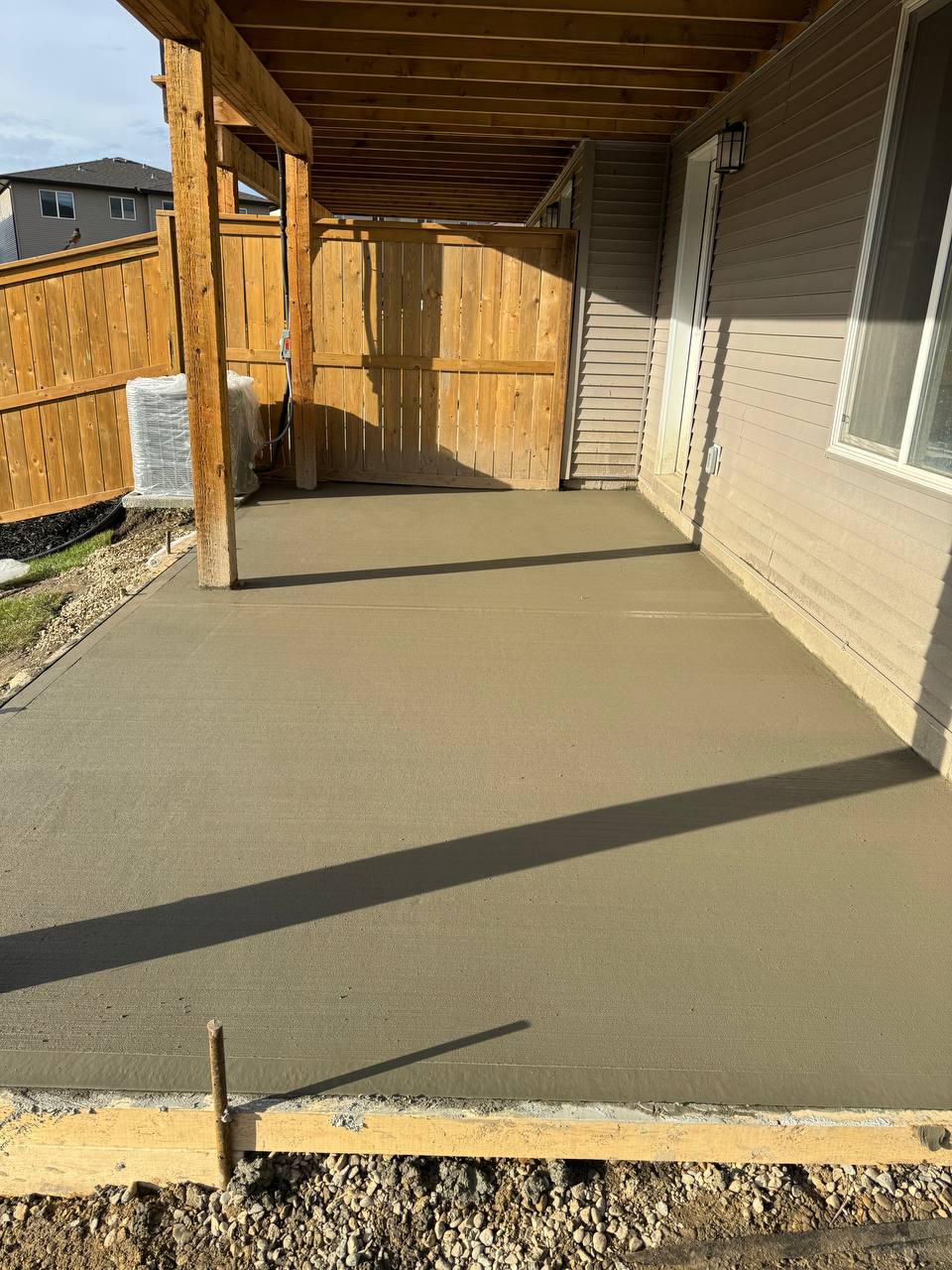 Newly poured concrete patio under covered pergola structure with wooden fence enclosure