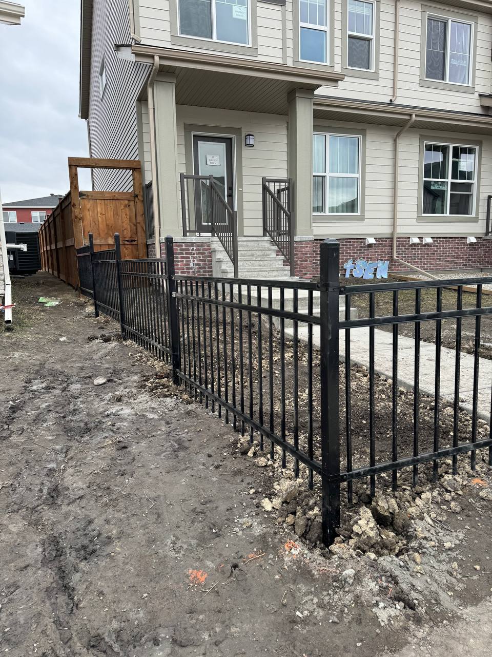 Black metal picket fence installation around residential property entrance with gravel base