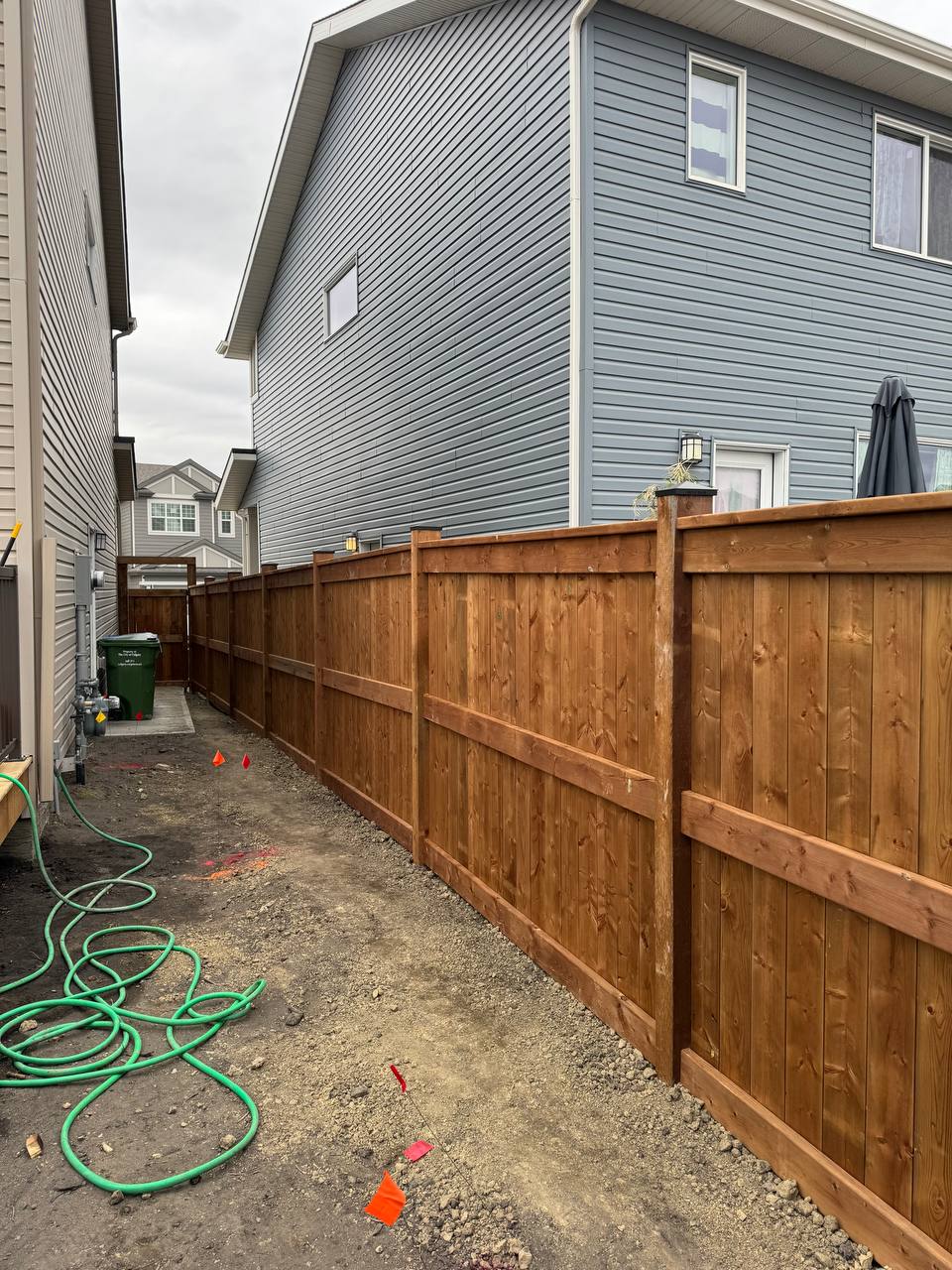 Wooden privacy fence installation in progress with construction markers and tools visible in residen