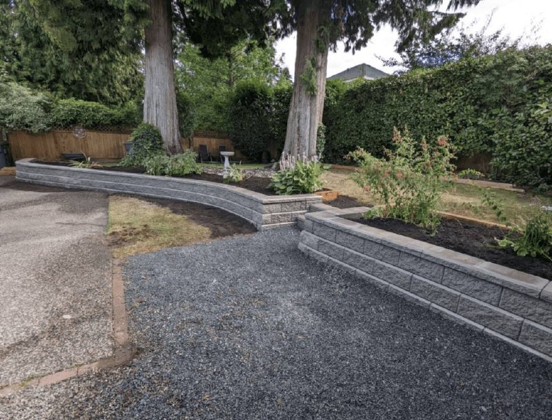 Curved dark gray segmental retaining wall installed around mature trees in residential backyard with