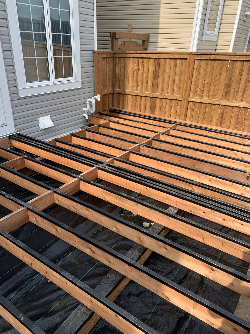 Deck framing in progress with joists and black moisture barrier installed