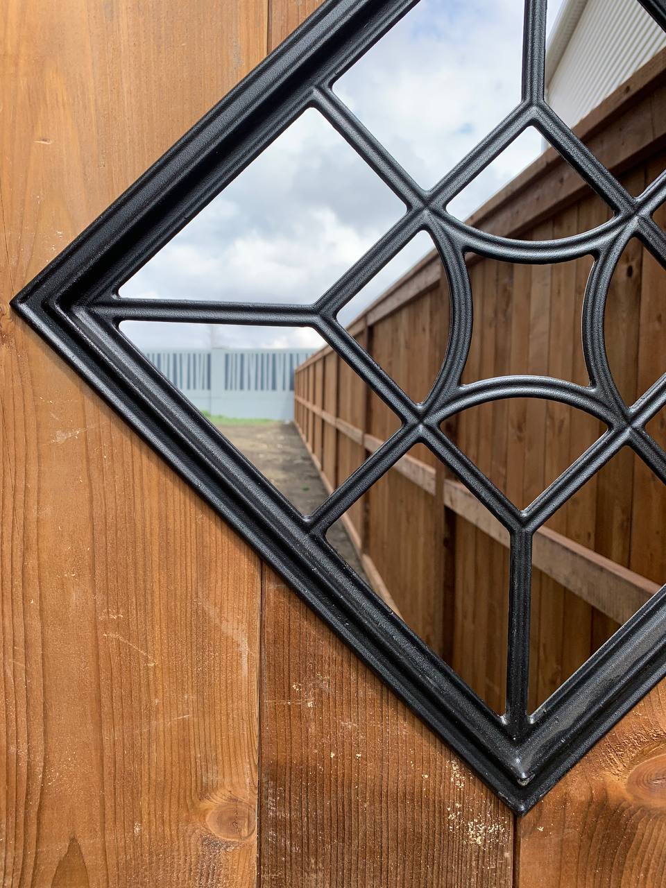 Decorative black wrought iron fence panel with geometric pattern mounted on wooden post