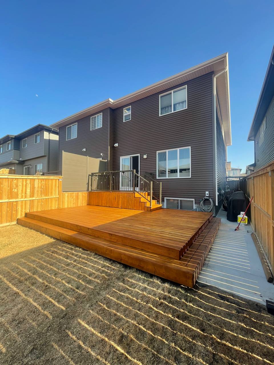 Newly constructed multi-level wooden deck with stairs and metal railing attached to modern home