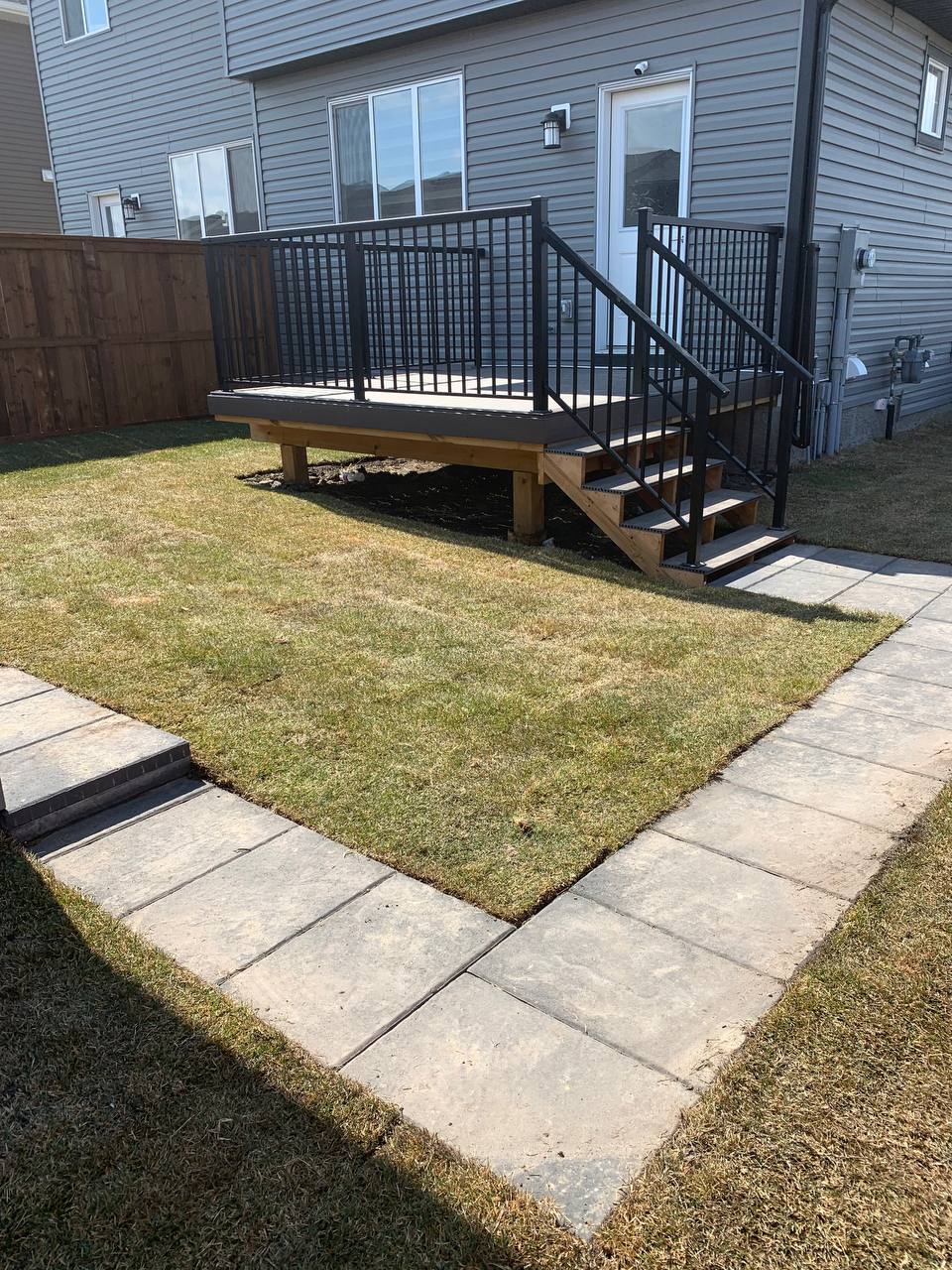Newly installed paver patio with fresh sod and elevated composite deck with black metal railings