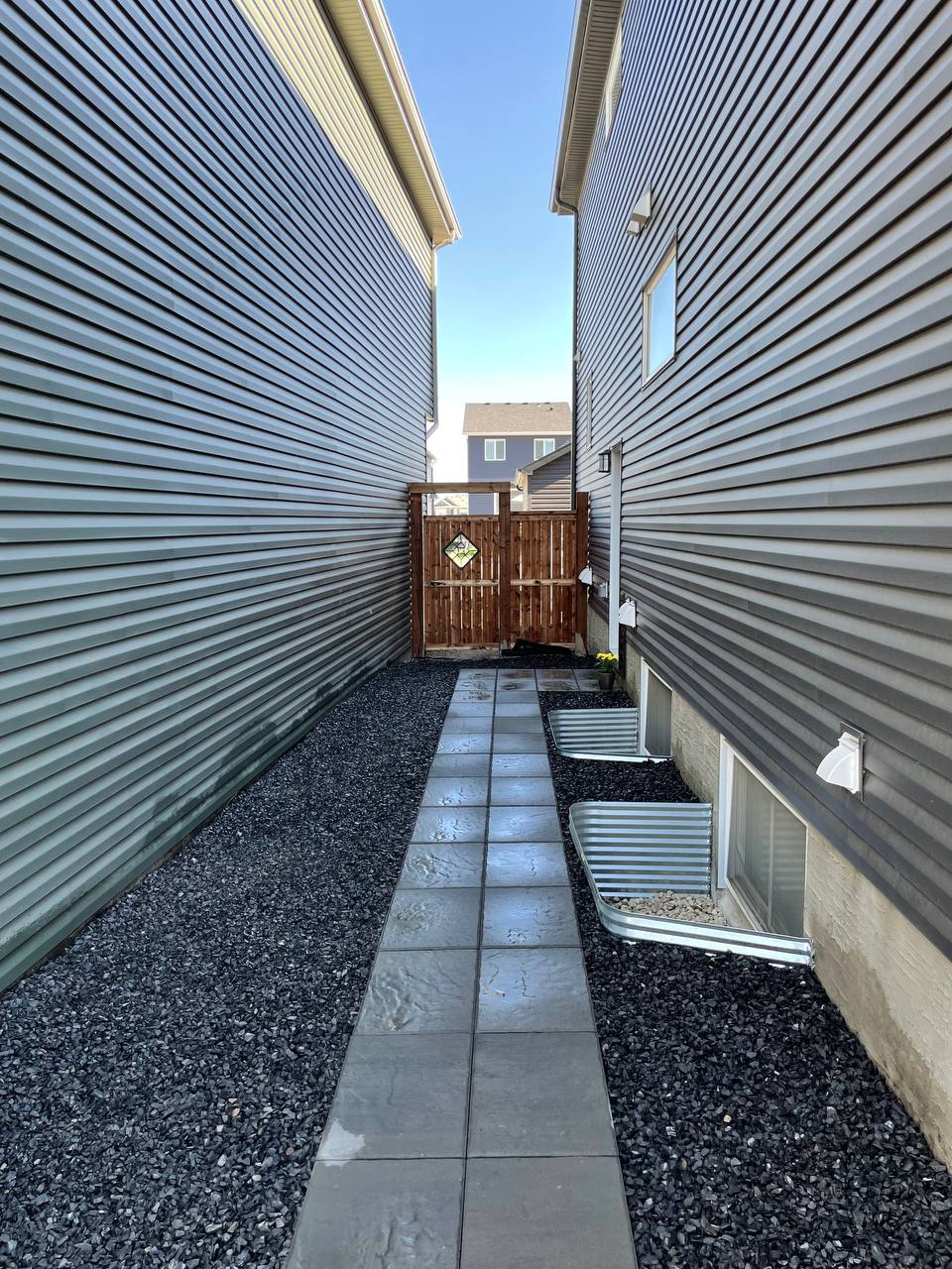 Finished narrow side yard with paved walkway, gravel landscaping, and metal planters between two res