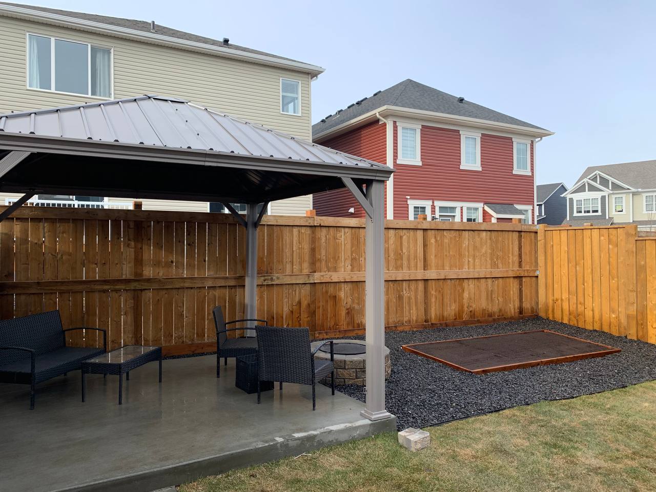 Backyard patio with pergola, concrete pad, gravel fire pit area, and wooden privacy fence