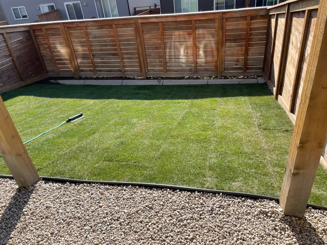 Newly installed artificial turf yard with gravel border and wooden fence enclosure