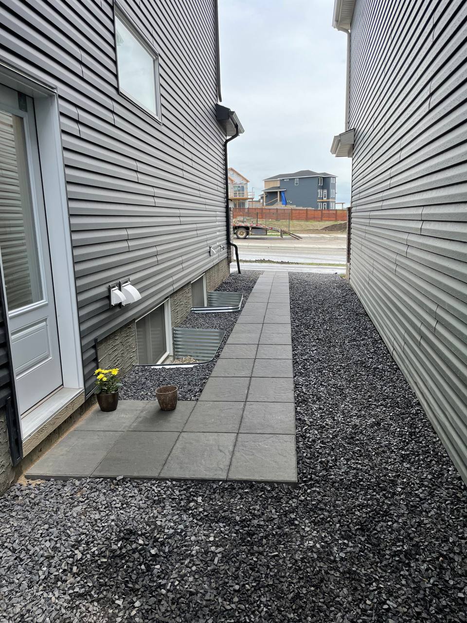 Completed narrow side yard pathway with paver walkway and gravel borders between two residential bui