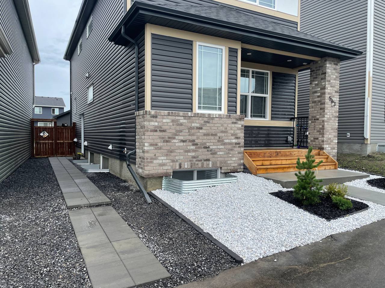 Modern front yard hardscape with paver walkway, decorative gravel, raised planter bed, and landscape