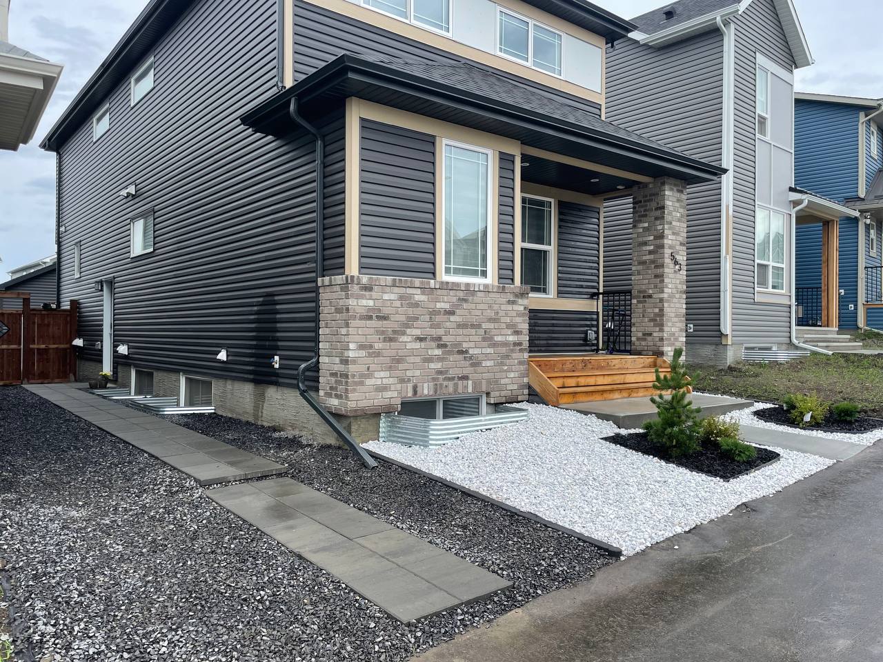 Modern front yard hardscape with decorative gravel, white stone accents, and wooden planter box