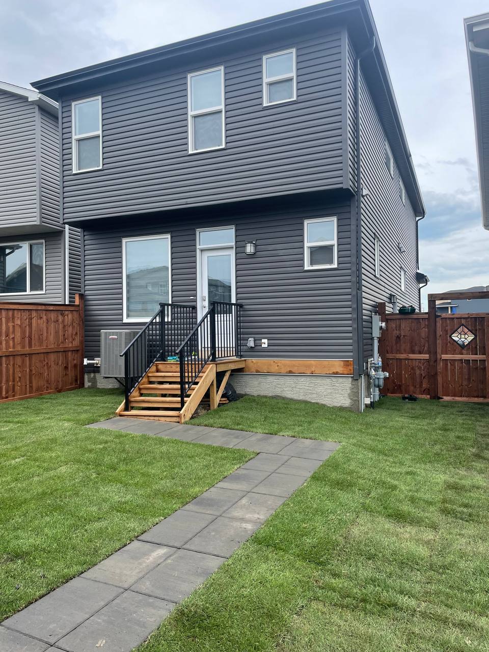 Modern residential backyard with concrete patio pathway, wooden deck steps, and manicured sod landsc