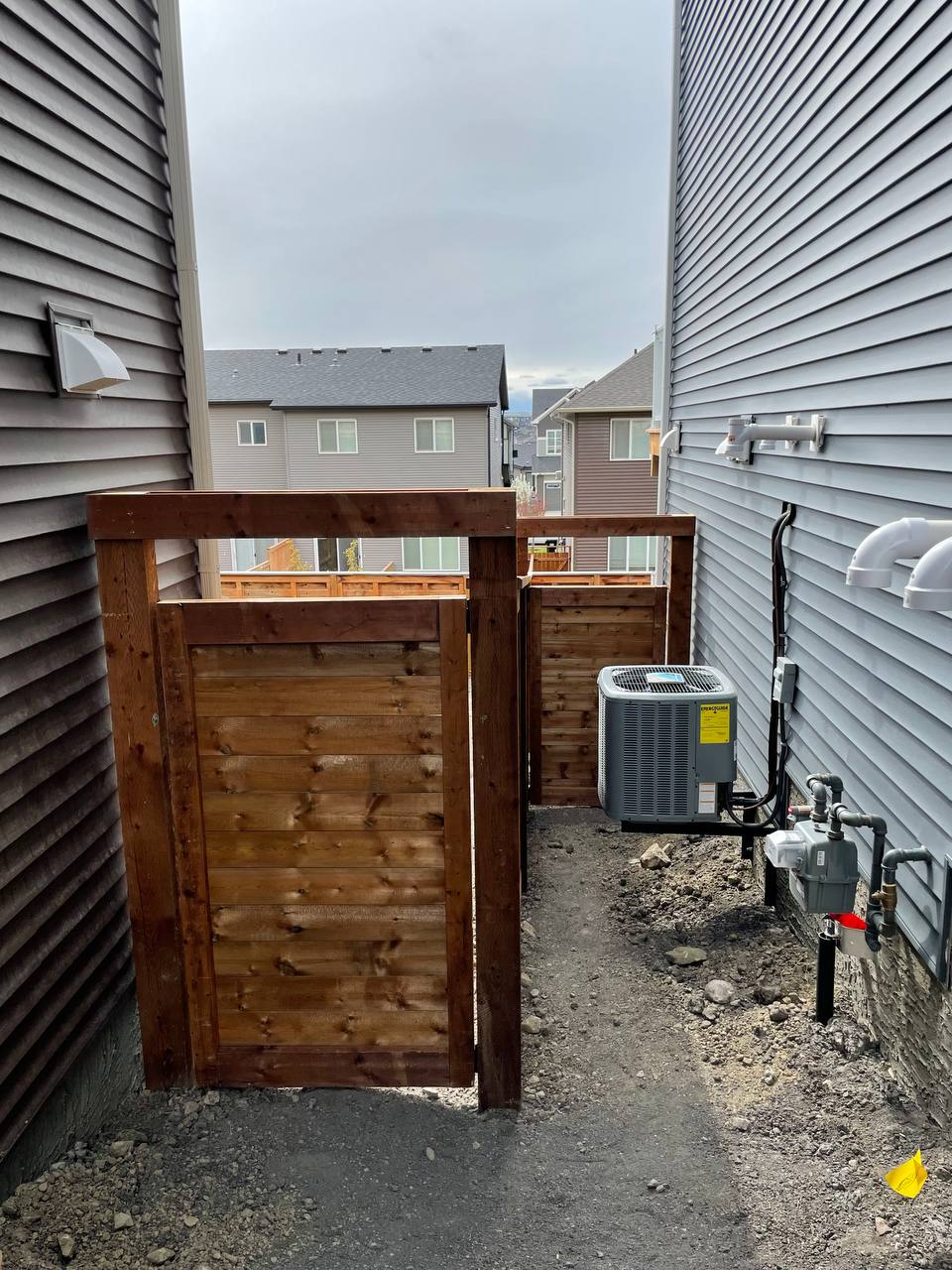 Wooden fence construction in progress between residential properties with HVAC unit and utility conn