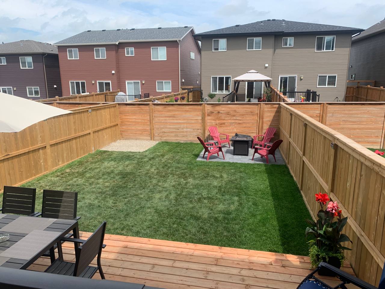 Finished backyard with new deck, sod, fire pit patio, and wooden fence in residential neighborhood
