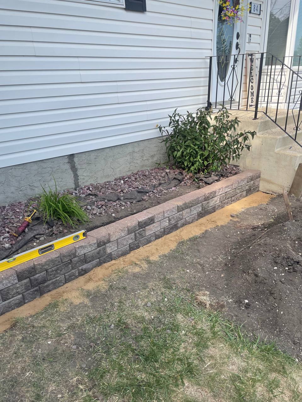 Retaining wall construction in progress with level tool visible and landscaping materials staged