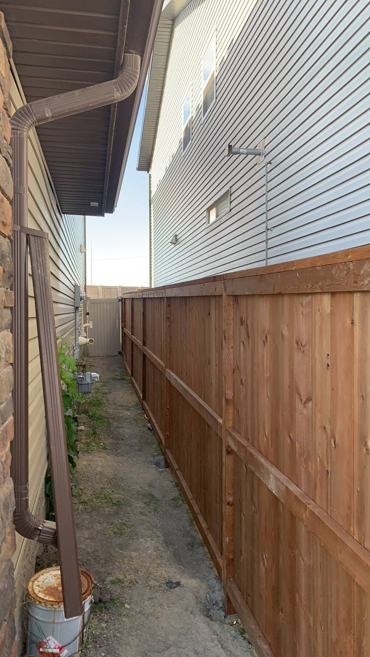 Completed wooden privacy fence installation between residential properties with metal railings on ad