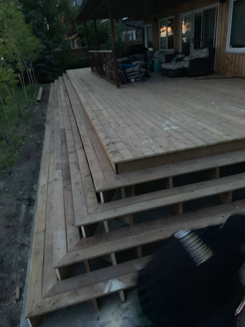 Wooden deck framing and decking installation in progress with house and patio visible in background