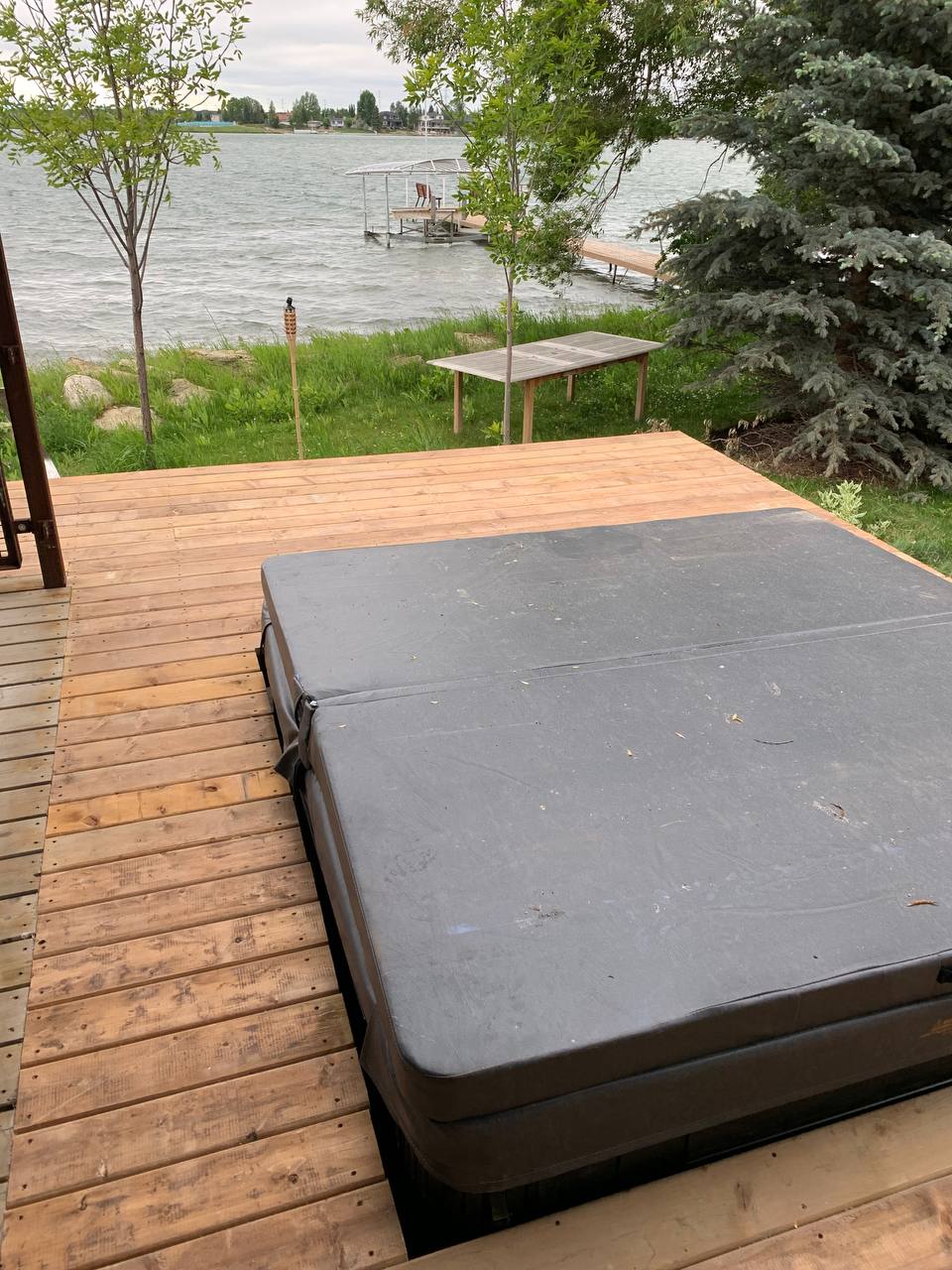 Finished waterfront deck with integrated hot tub and landscaping overlooking lake