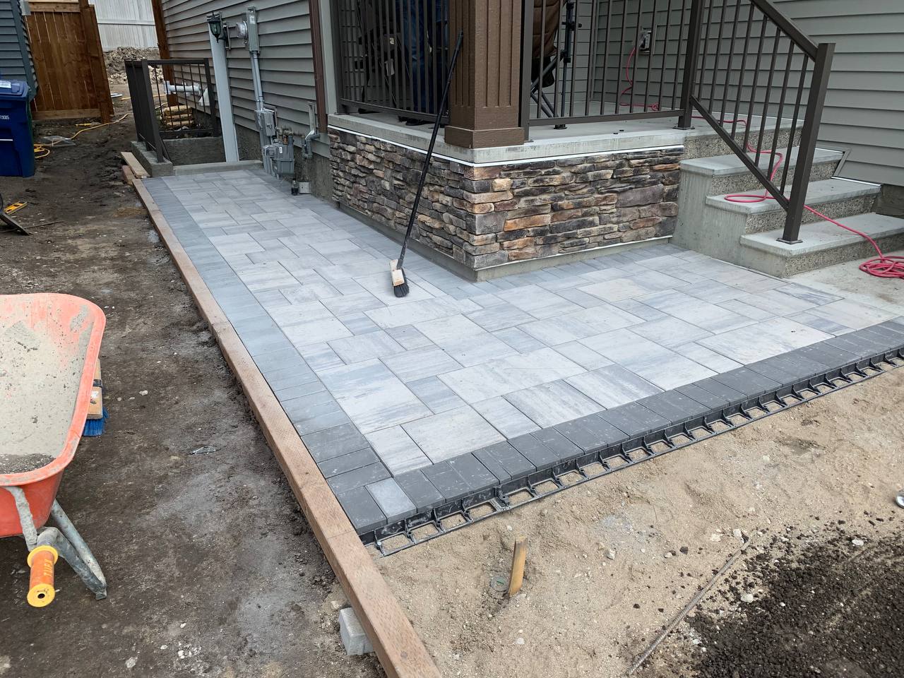 Patio installation in progress with pavers being laid in herringbone pattern and edging being instal