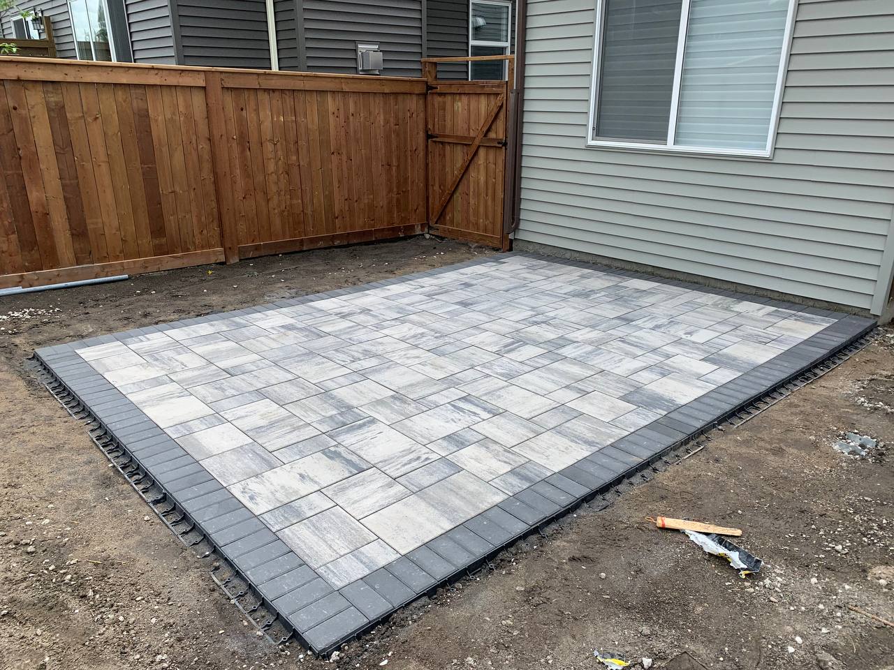 Completed paver patio with dark border edging in residential backyard