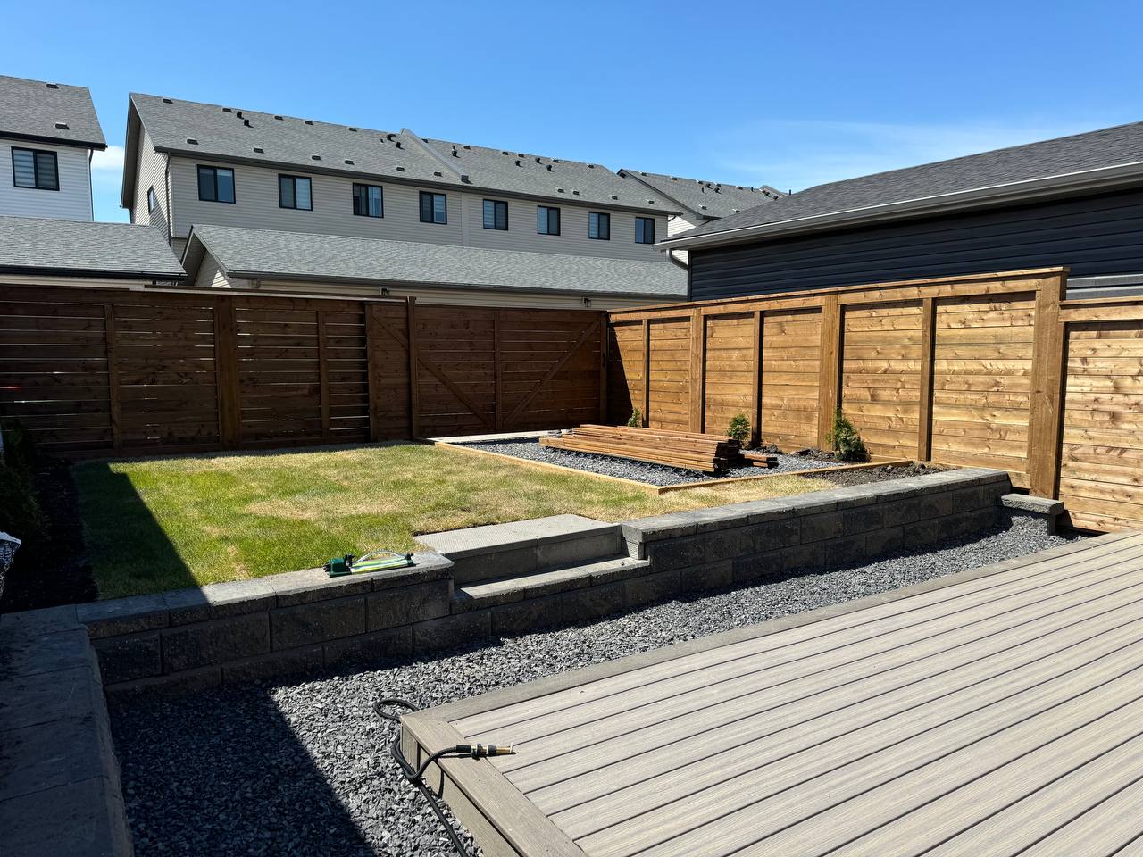 Completed backyard hardscape with composite deck, retaining walls, gravel beds, and wooden privacy f